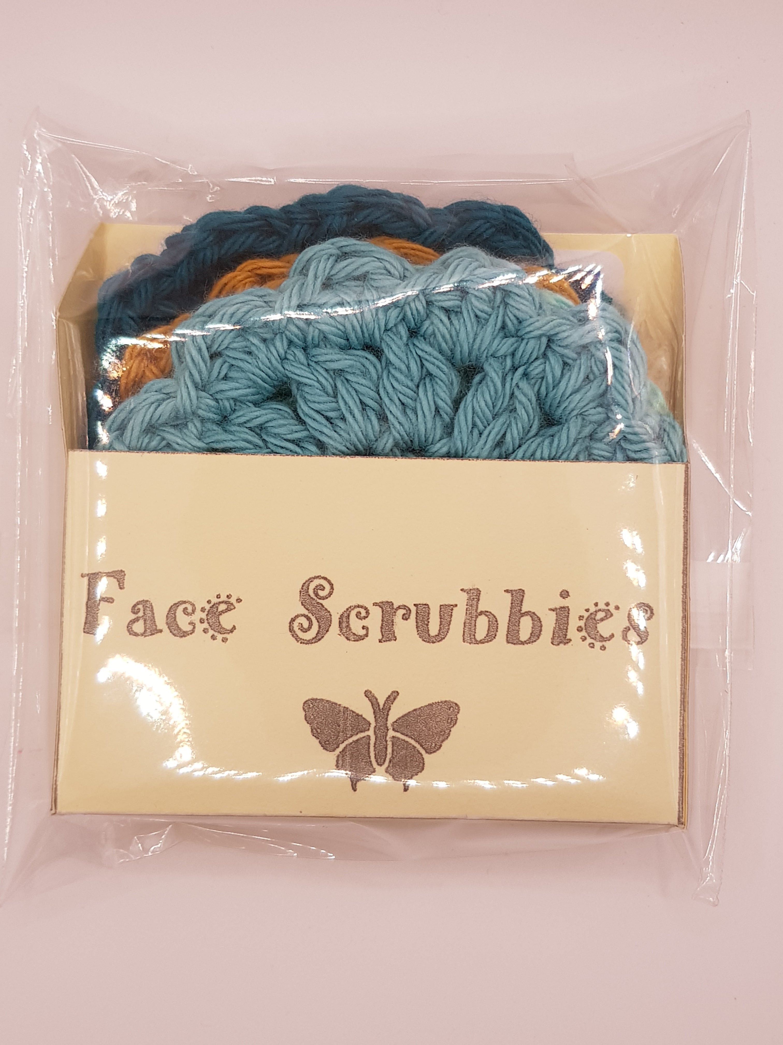 A set of jean & andy cotton reusable face scrubbies in blue and orange hues, packaged in a cream-colored box featuring a butterfly logo and the text "Face Scrubbies." The environmentally sustainable scrubbies are visible through the transparent wrapping.