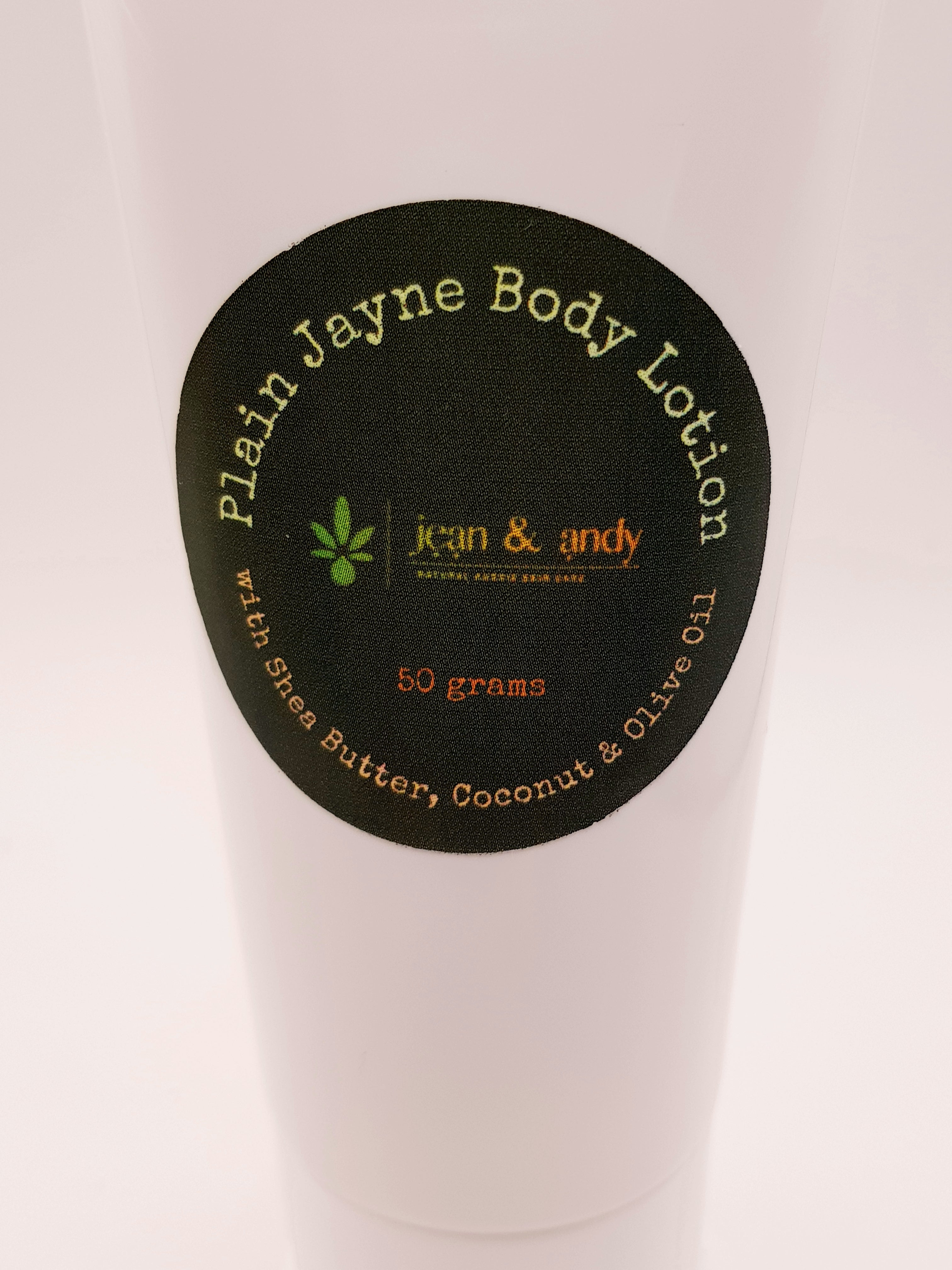 A 50-gram white bottle features a round black label with "Plain Jayne Body Lotion" by jean & andy. Infused with shea butter, coconut, and olive oil, this lotion provides skin hydration and antioxidant protection.