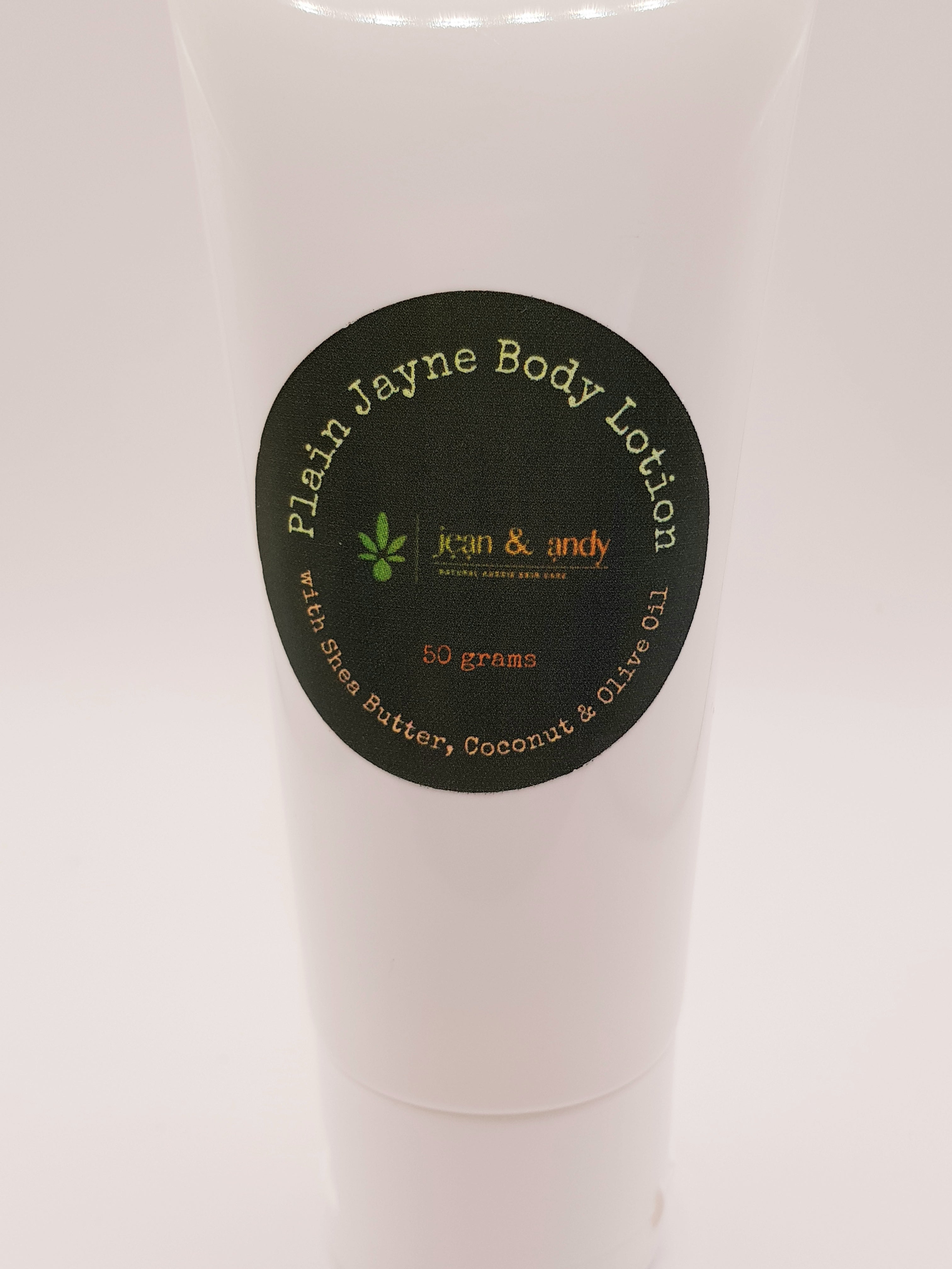 A 50-gram tube of jean & andy's Plain Jayne Body Lotion comes in white with a black circular label, featuring green and orange text. Enriched with Shea Butter, Coconut, and Olive Oil, this lotion enhances skin hydration and provides antioxidant protection.