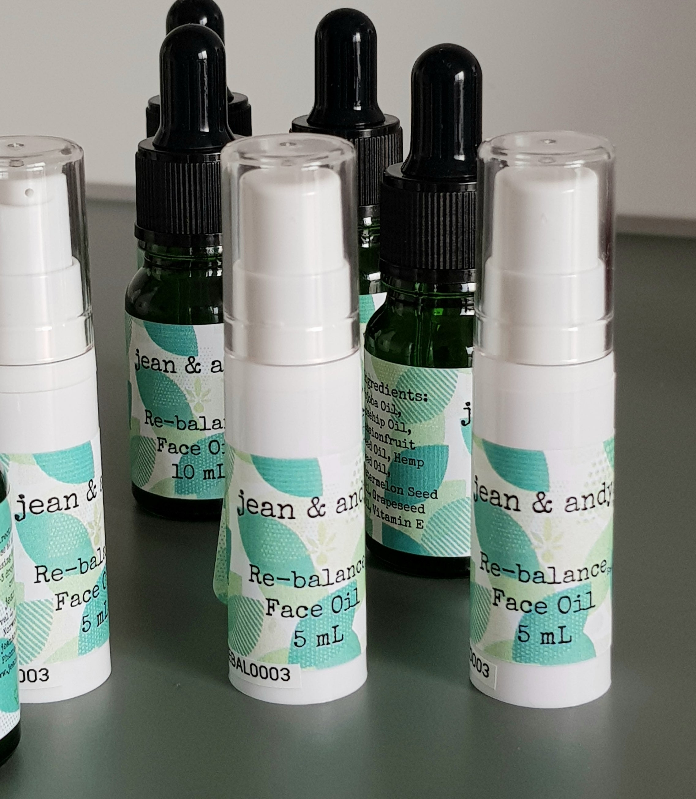 A close-up of multiple bottles of jean & andy's Re-balance Face Oil for acne/combination skin, each marked with 5 mL on the front. The bottles vary in size and feature clear caps, all arranged neatly on a smooth surface.