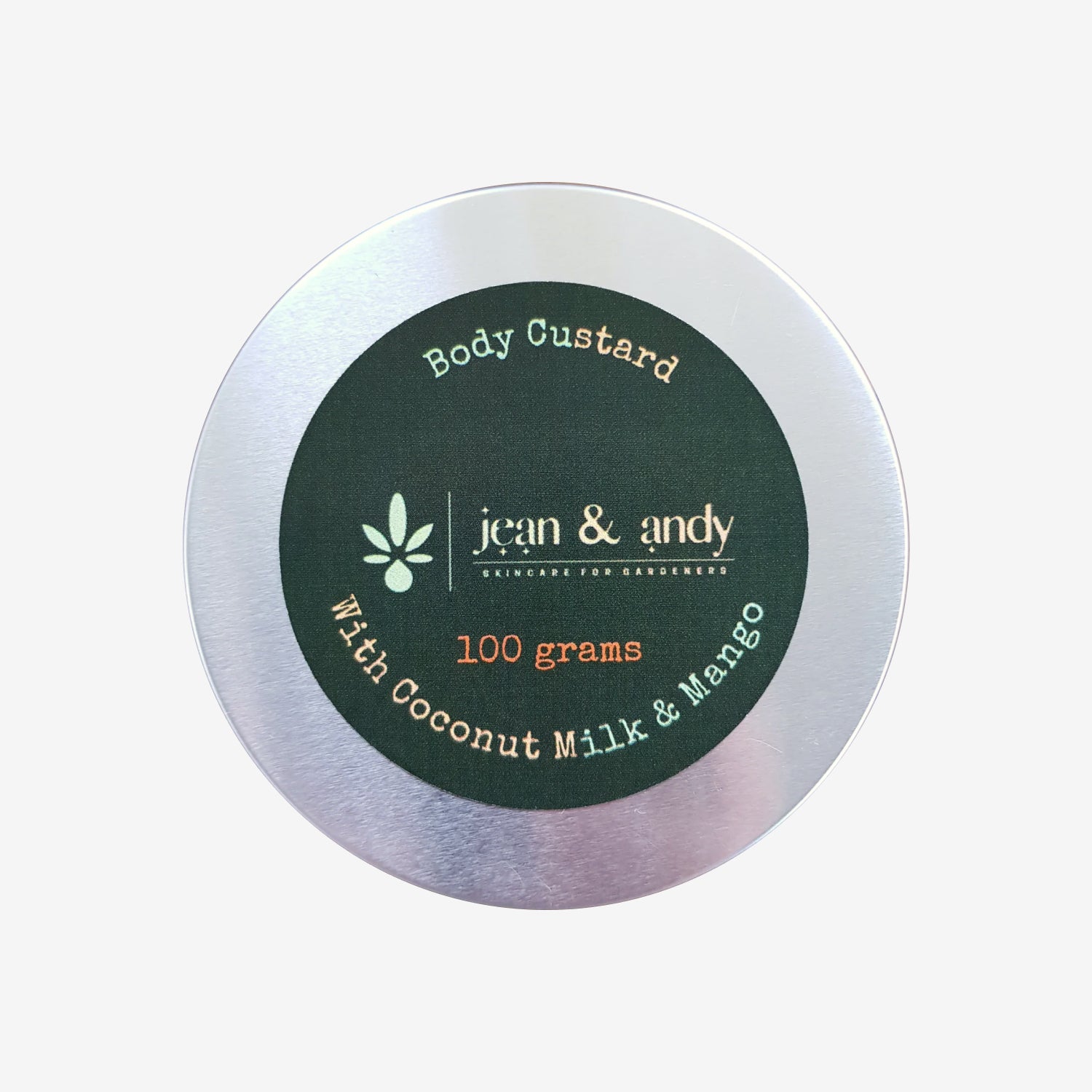 A circular tin of Body Custard featuring a silver lid has a dark green label that reads jean & andy, Body Custard with Coconut & Mango, 100 grams, enriched with Coconut Oil & Mango, along with a small leaf graphic.