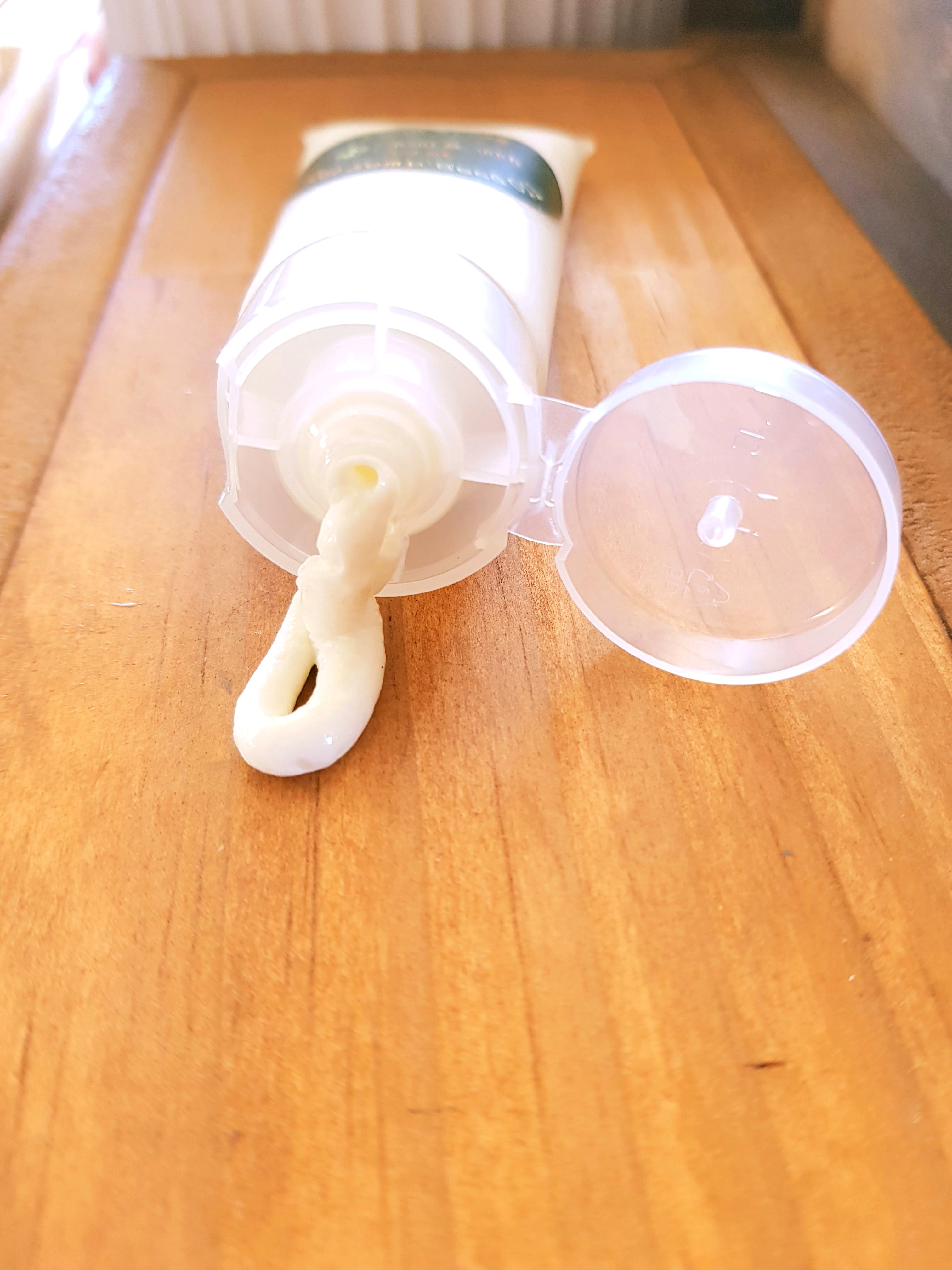 A tube of jean & andy Hand Cream with Hemp Seed Oil sits on a wooden surface, its cap open, releasing a small dollop of thick, white cream perfect for sensitive skin.
