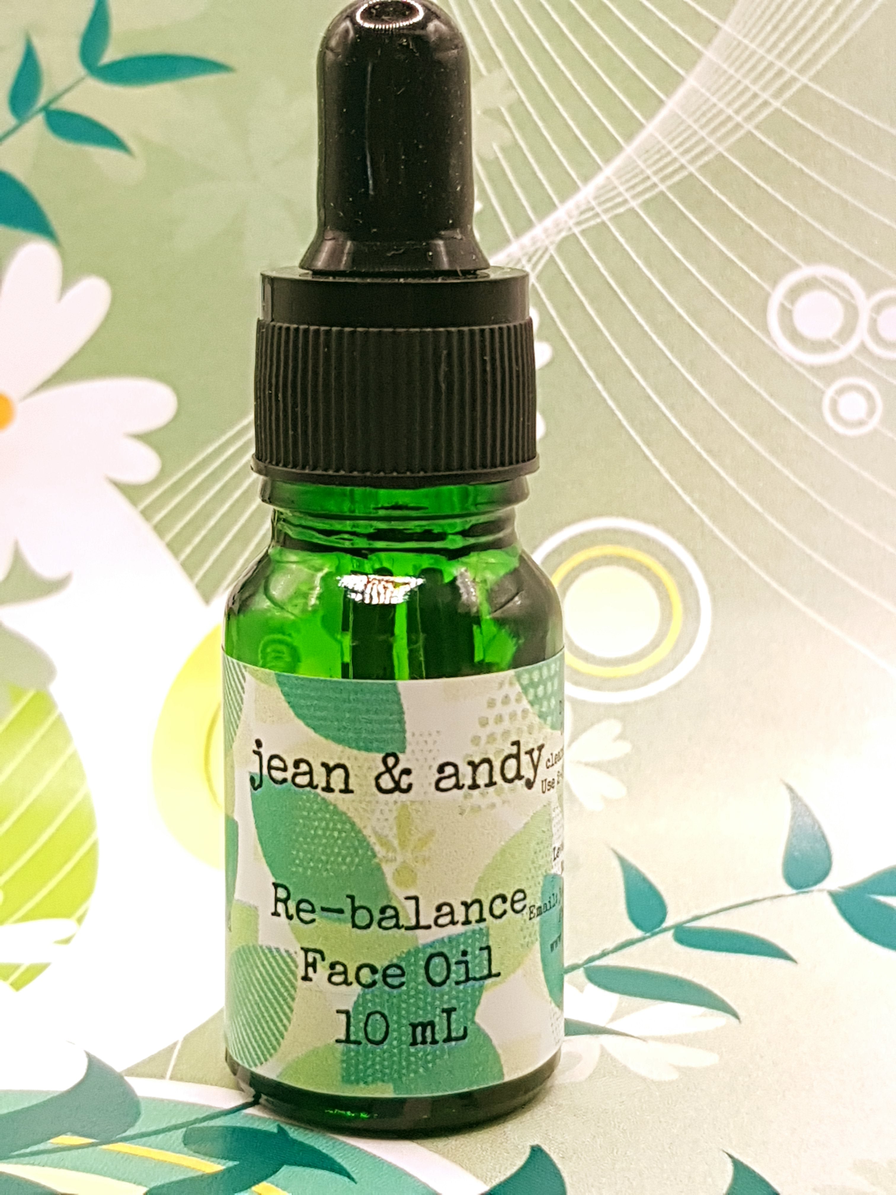 A compact 10 mL green bottle of jean & andy's Re-balance Face Oil for acne/combination skin, featuring a black dropper cap. This product is perfect for those with acne-prone skin, harnessing the power of linoleic acid. The backdrop is decorated with abstract floral and leaf motifs in green and white hues.